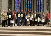 13 Frauen stehen im Halbkreis im Altarraum der Heiliggeistkirche in Frankfurt. Im Hintergund: bunte Glasfenster