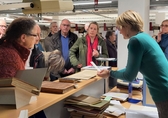 Besuchergruppe steht um den Tresen der Metereologischen Bibliothek und blickt auf Dokumente, die ihr die Leiterin zeigt