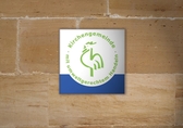 Plakette mit Logo Grüner Hahn hängt an einer Hauswand