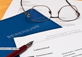 blaube Bewerbungsmappe, Kugelschreiber und Brille  liegen auf einem Tisch. Die Bewerbung ist noch in Bearbeitung. Foto: AdobeStock 99816806t auf einem Tisch