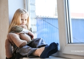 Mädchen sitzt mit Teddy auf Fensterbank